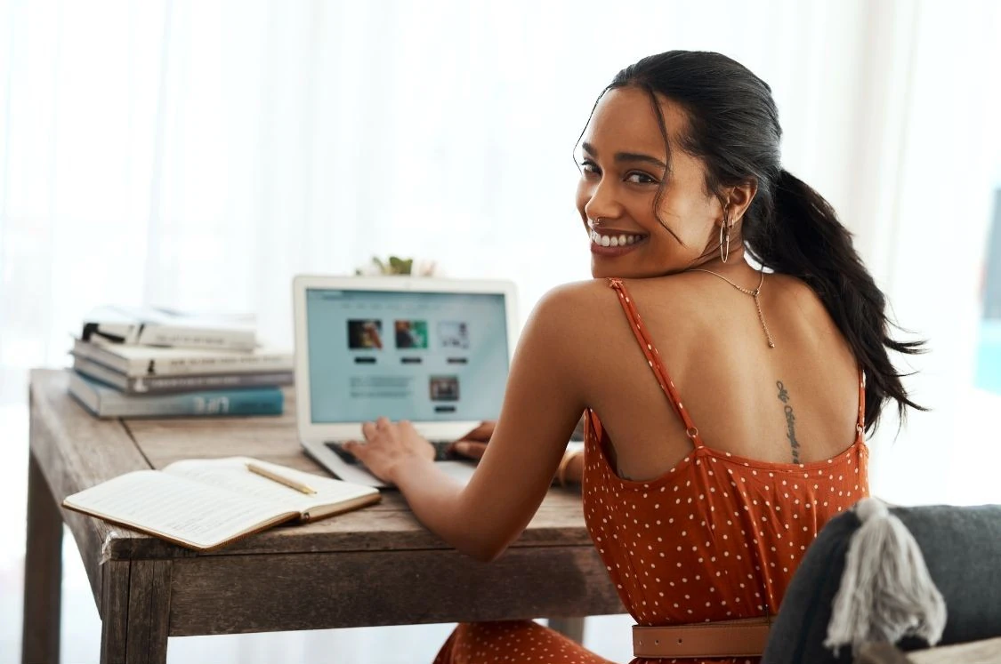 Femme entrepreneure assise à un bureau qui travaille sur son site en souriant.